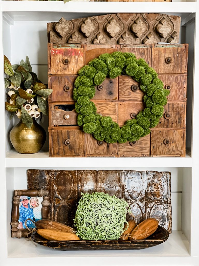 built in shelving styled with natural elements including green moss wreath, moss ball, dough bowl, antique drawer set, and rusted metal