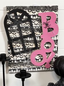 DIY Handmade Halloween Sign: A charming Halloween decoration featuring a spider web adorned with fake spiders. The word 'boo!' is creatively crafted from pink scrap paper, set against a playful black and white ghost background.