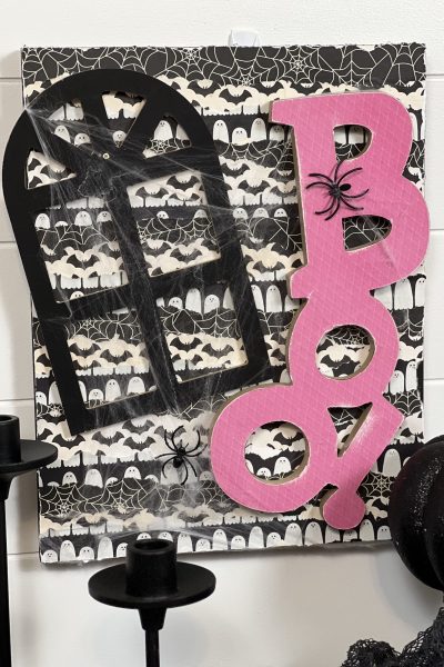 DIY Handmade Halloween Sign: A charming Halloween decoration featuring a spider web adorned with fake spiders. The word 'boo!' is creatively crafted from pink scrap paper, set against a playful black and white ghost background.